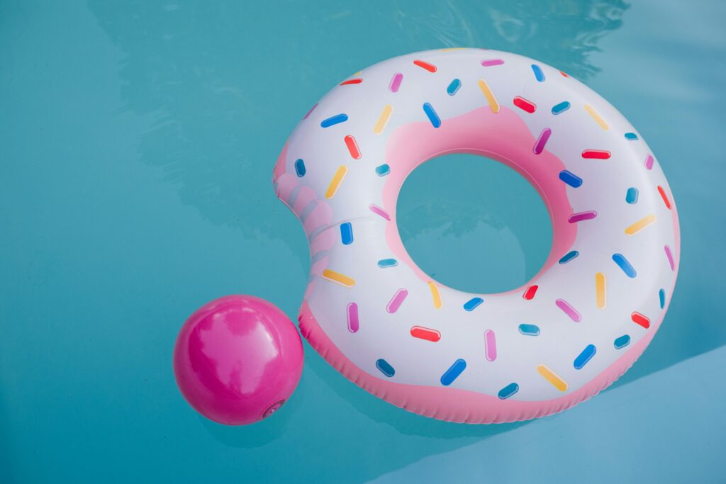A vibrant donut-shaped inflatable floats beside a pink ball in a clear blue pool.